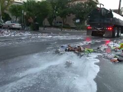 Medium Shot Tilt Down - Garbage truck sprays street with water as it drives down street; sudsy water in road / New Orleans Louisiana Stock Footage