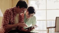 Young couple talk and laugh while browsing tablet computer on motel bed Stock Footage