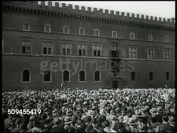 1936: LEAGUE OF NATIONS: POST WAR: LA WS Benito Mussolini standing on balcony. HA WS Italian crowds cheering on street, Rome, Italy. WS Cars arriving at League of Nations building, Geneva, Switzerland. INT VS League members in corridor, room, talking. Instructional Video