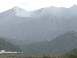 Car drives beneath smoking crater of volcano kicking up large cloud of dust, Japan Stock Footage
