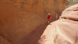 Young hiker boy and young hiker girl run past with their mother down a trail in a narrow red-rocked canyon Stock Footage