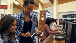A young African American female librarian assists college or high school student in library computer lab Stock Footage