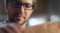 Young artisan in workshop polishes skateboard with sandpaper and blows away wood shavings Stock Footage