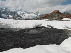 Creek flows from snowpack towards distant mountains Stock Footage