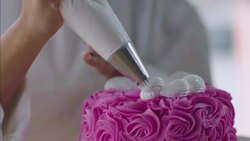 Pastry chef decorates pink cake with white icing designs Stock Footage