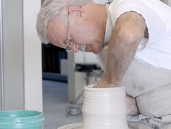 MS TS senior potter sits at pottery wheel shaping wet clay with his bare hand / Palm Springs, California, USA Stock Footage
