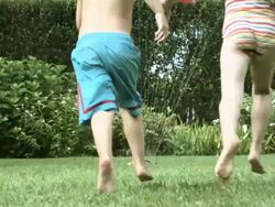 Boy and girl jumping through water from garden sprinkler Stock Footage