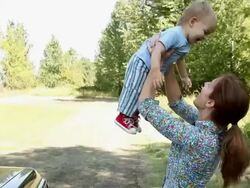 Mother lifting baby son off car hood and spinning him around Stock Footage
