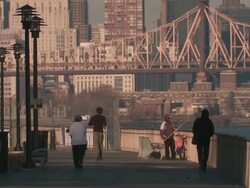 People jogging, walking, and fishing on a path along the east river in manhattan with the queensboro bridge in the background late in the day Stock Footage