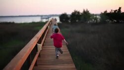 Two boys run down a boardwalk near the ocean. Stock Footage