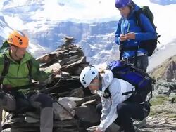 Boom shot of three mountaineers building rock cairn, taking cell phone pics Stock Footage
