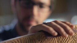 Young carpenter brushes curve of wooden skateboard with sandpaper Stock Footage