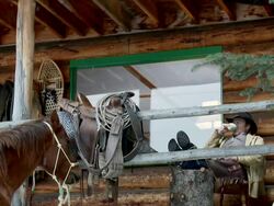 Cowboy sits on porch outside log cabin Stock Footage