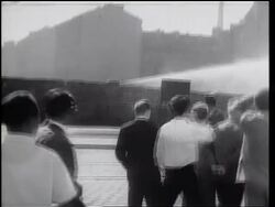 B/W 1961 long shot hose spraying water from top of Berlin Wall / REAR VIEW of people watching in foreground Stock Footage