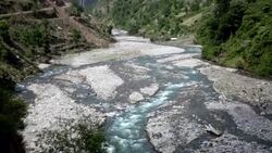 Pan shot of vast braided river valley with tent camp and Himalayan Mountains in background. Stock Footage