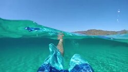 SLOW MOTION: Young male tourist in blue shorts kicking and swimming in the sea. Stock Footage