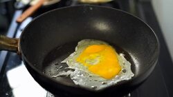 slow-motion of hand cracking egg dropping into a frying pan Stock Footage