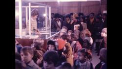 1970s: Woman writes on clipboard and speaks to children gathered in front of counter Stock Footage