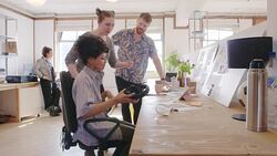 Creative designers discussing photograph proofs in open plan office Stock Footage
