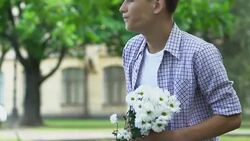 Boy holding flowers, waiting for girlfriend on date, nervous, insecure teenager Stock Footage