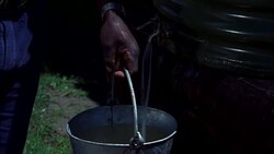 CLOSE ANGLE OF A MAN HOLDING A BUCKET UNDER BARREL, FILLING IT WITH WATER FROM THE BARREL. MAN TURNS SPOUT OFF AND WALKS AWAY. Stock Footage