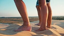 closeup of the legs of a young woman and man enjoying the sunset on the peak of one of the desert sand dune Stock Footage