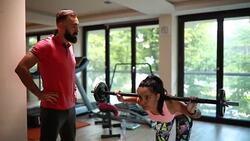 Woman exercising with a barbell in front of her personal coach Stock Footage