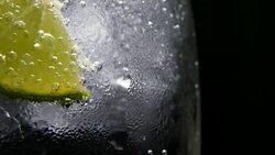 Macro close-up,refreshing soda tonic fizzy water, lime in Glass, ice. Slice of lemon, mineral bubbles. Detox or thirst concept. Healthy, dietary nutrition. Cold lemonade mojito drink. Black background Stock Footage