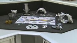 McLaren F1 car parts in display cases with engineers working in background News Clip