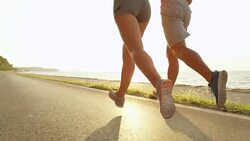SLOW MOTION: Athletic young woman and man running down a scenic coastal road. Stock Footage