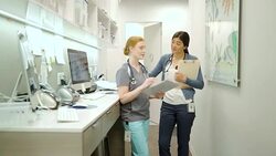 Female doctor and nurse discussing medical chart at clinic nurses station Stock Footage