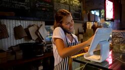 Beautiful young waitress registering a delivery on system while talking to customer on phone Stock Footage