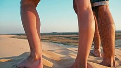 closeup of the legs of a young woman and man enjoying the sunset on the peak of one of the desert sand dune Stock Footage