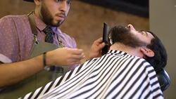 Young barber trimming beard of client in salon Stock Footage
