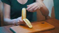 Woman Cleaning a Banana While Sitting at a Table in a Home Kitchen Stock Footage