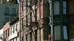 UP ANGLE OF LOWER CLASS BRICK APARTMENT BUILDING WITH FIRE ESCAPES. URBAN AREA. STOPLIGHT IN FG. Stock Footage