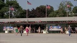 WIDE ANGLE OF ENTRANCE TO MONMOUTH PARK, HORSE RACING TRACK IN OCEANPORT, NEW JERSEY. SIGN FOR THE FOURTH OF JULY DERBY. PEOPLE, PEDESTRIANS, SPECTATORS. AMERICAN FLAGS. Stock Footage