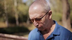 An elderly man with glasses reading an e-book on a Park bench Stock Footage
