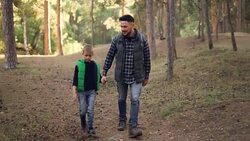 Caring father is hiking with his child in forest on sunny autumn day, man and boy are walking and talking holding hands. Parenthood and childhood concept. Stock Footage