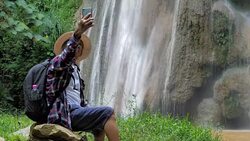 Senior man Asian traveler sitting enjoying and selfie with smart phone in front of the waterfall. Lifestyle Travel, Technology and Relaxation concept Stock Footage