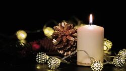Close up Christmas candle with pine cone,fir,mistletoe and vintage light string on black table at night Stock Footage