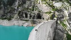 Aerial view of white camper van crossing dam in Swiss Alps Stock Footage