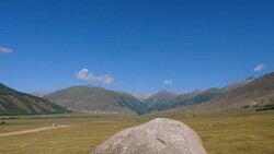 Big stone in green meadow in highlands landscape and mountain peaks on blue sky Stock Footage