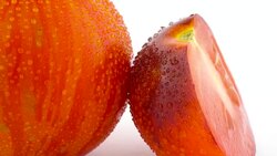 Macro shooting of one whole red globe striped tomato and one half of indigo rose tomato slowly rotating on the turntable isolated on the white background. Stock Footage