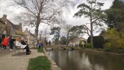 People walking along riverbank in Bourton on the Water News Clip
