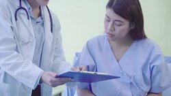 Beautiful smart Asian doctor and patient discussing and explaining something with clipboard in doctor hands while staying on Patient's bed at hospital. Medicine and health care concept. Stock Footage