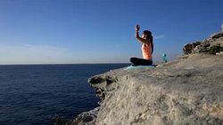 Young woman sitting on the cliff near the sea practicing yoga Stock Footage