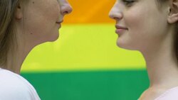 Passionate kiss of two beautiful lesbians on rainbow flag background, close-up Stock Footage