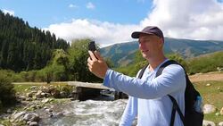 Man using smart phone for video chat while travel in mountain with rapid river Stock Footage