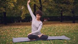 Slender girl is doing yoga exercises for healthy spine stretching body and arms then relaxing in lotus position with hands on kness and closed eyes. Youth and meditation concept. Stock Footage